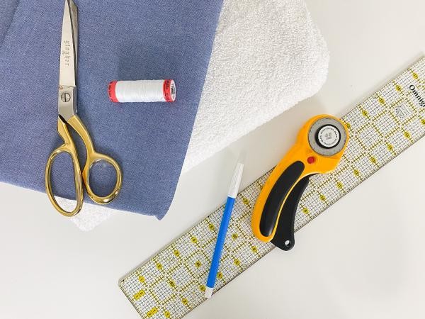 Materials laid out for sewing a travel changing pad: towel, fabric, ruler, rotary cutter, mat, scissors, pins, pen, thread, and BERNINA sewing machine.