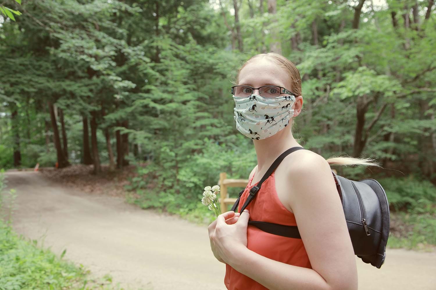 Woman wearing a face mask walking in a forest, highlighting personal safety and health considerations while traveling