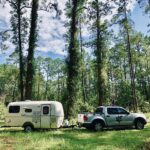 A woman standing in front of her Casita travel trailer in a scenic outdoor location.