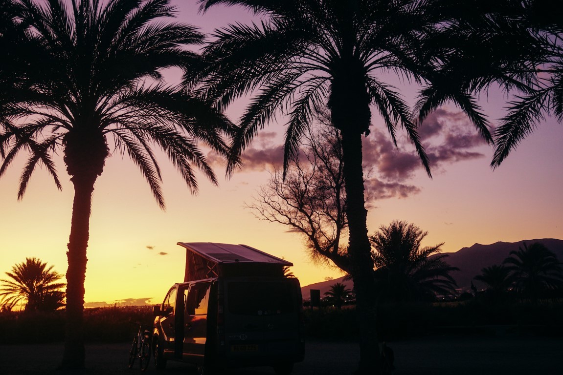 camper van at purple and yellow sunset parked between palm trees