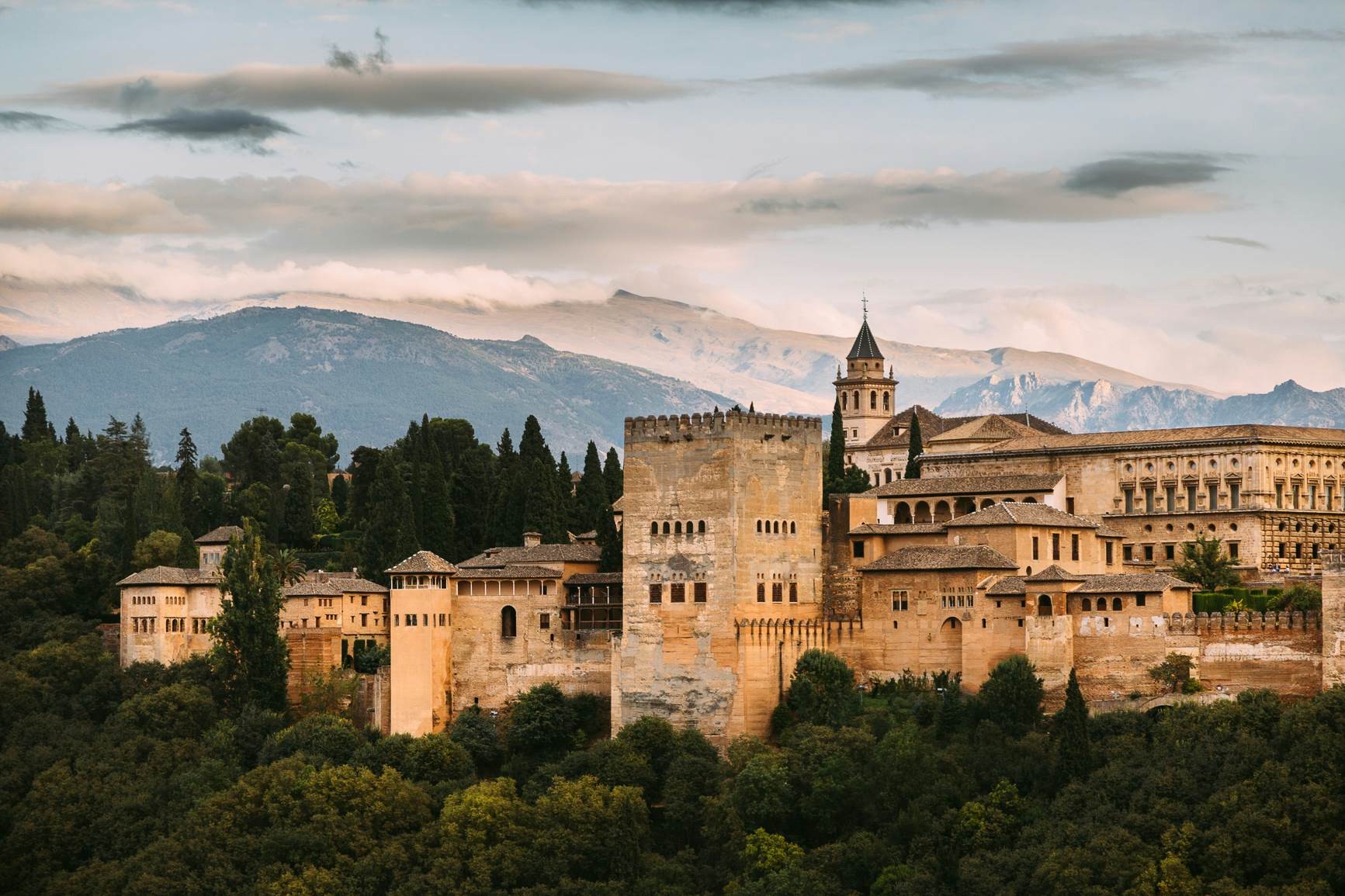 The large palace of the Alhambra sits on a hill with mountains in the background.