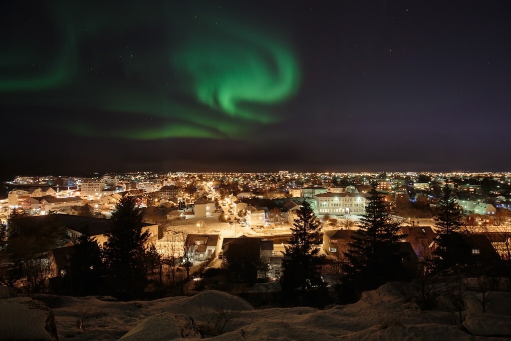 The Northern Lights, a breathtaking green aurora borealis, dance across the night sky above Reykjavik, Iceland, illuminating the city.