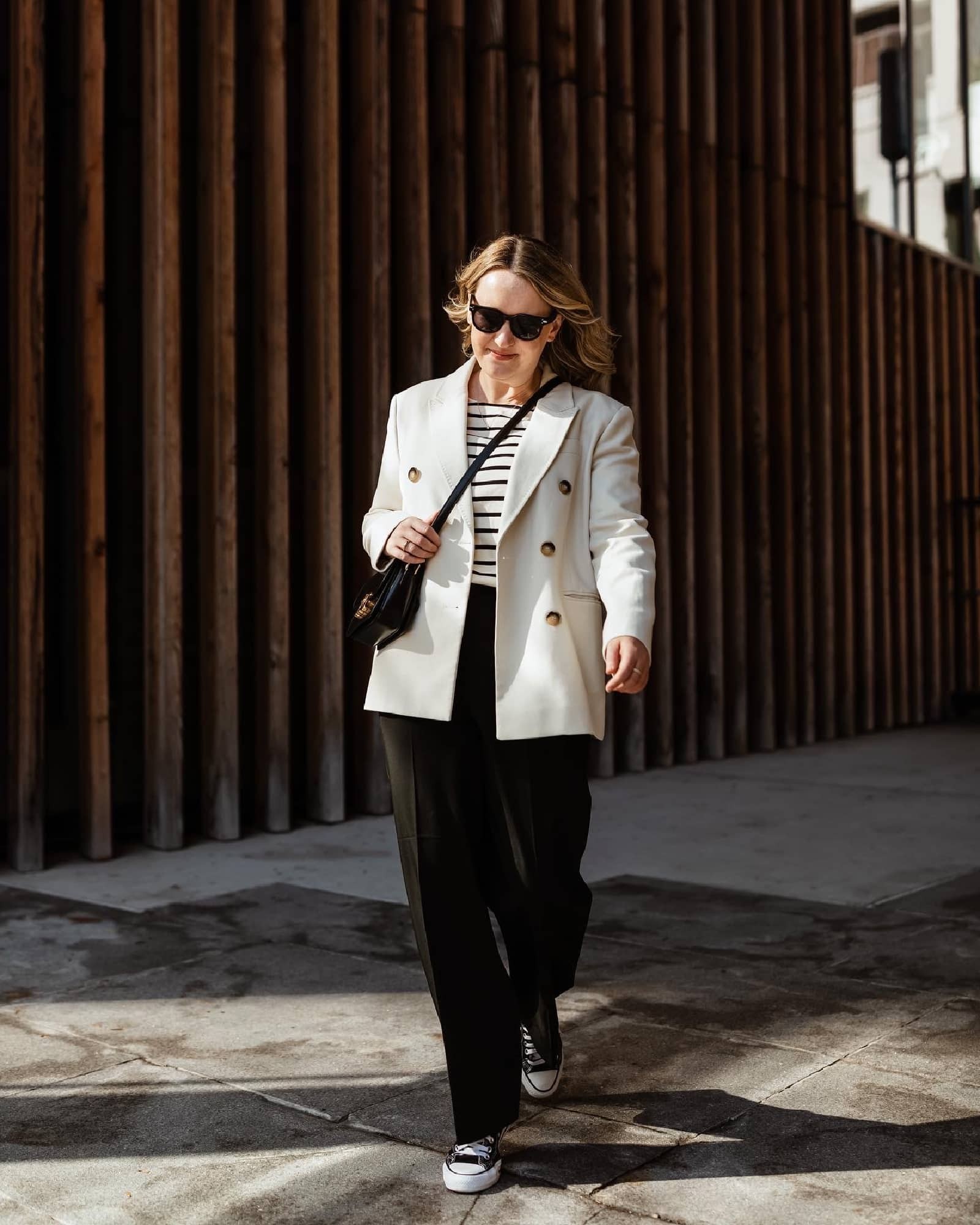 Woman wearing blazer, striped tee, black trousers and converse sneakers, demonstrating packing tips for Europe