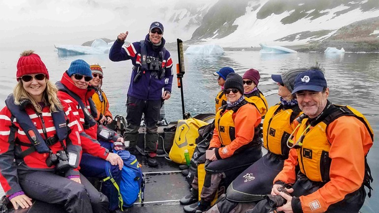 A group in a zodiac boat explores the waters around Cuverville Island, Antarctica, surrounded by ice and snow.