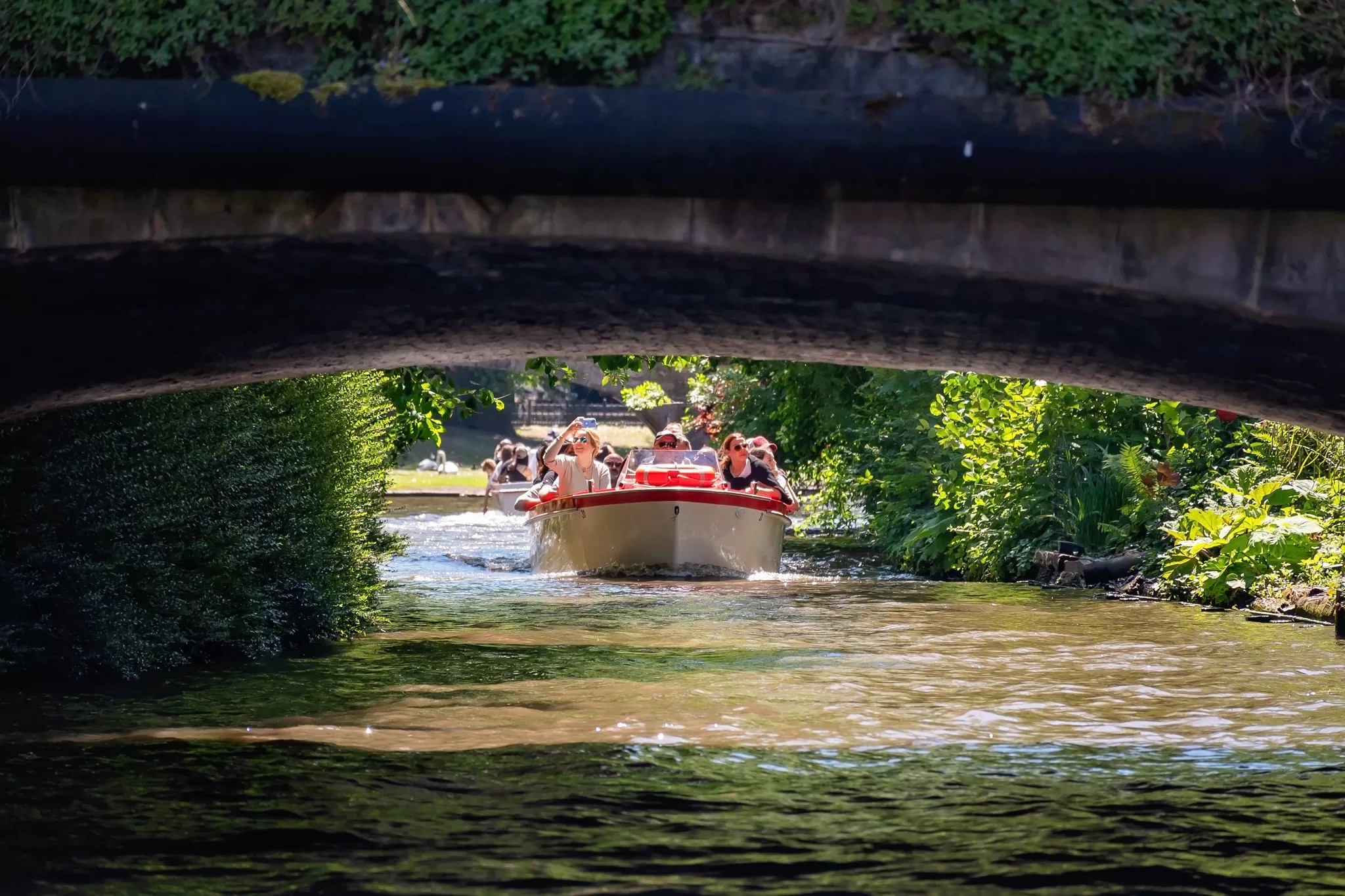 a red and white canal tour boat in Bruges about to go under a bridge