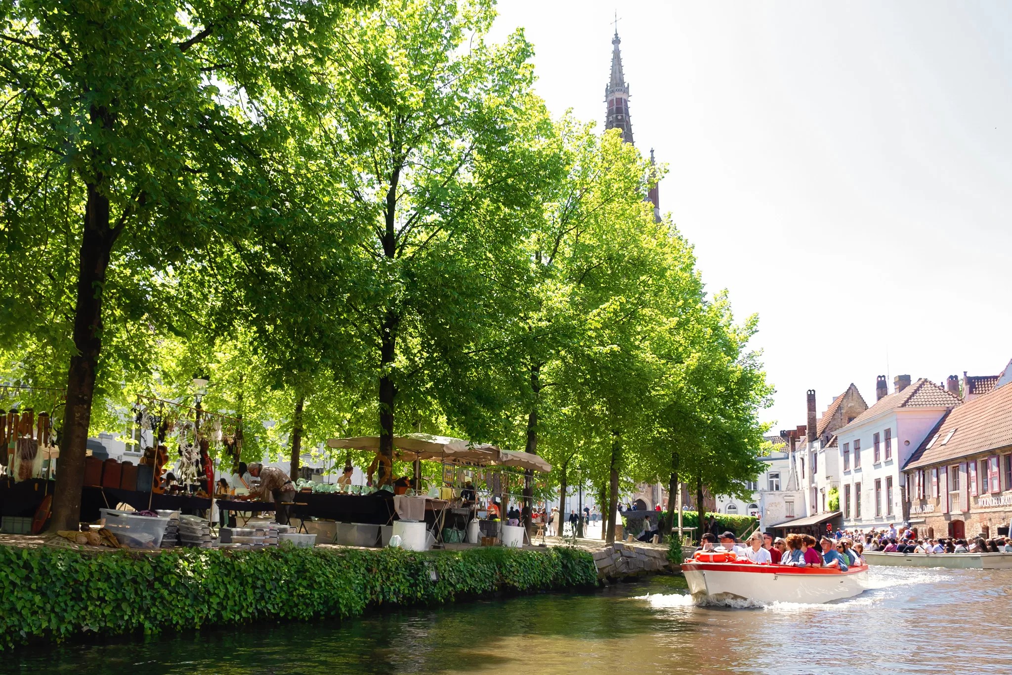 This image shows a photo of a boat cruising along the canals in Bruges. The blog post is about a Bruges 1 day itinerary 