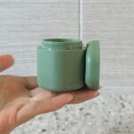 Close-up of a hand holding a medium-sized Cadence Capsule, showcasing its compact design for travel toiletries.