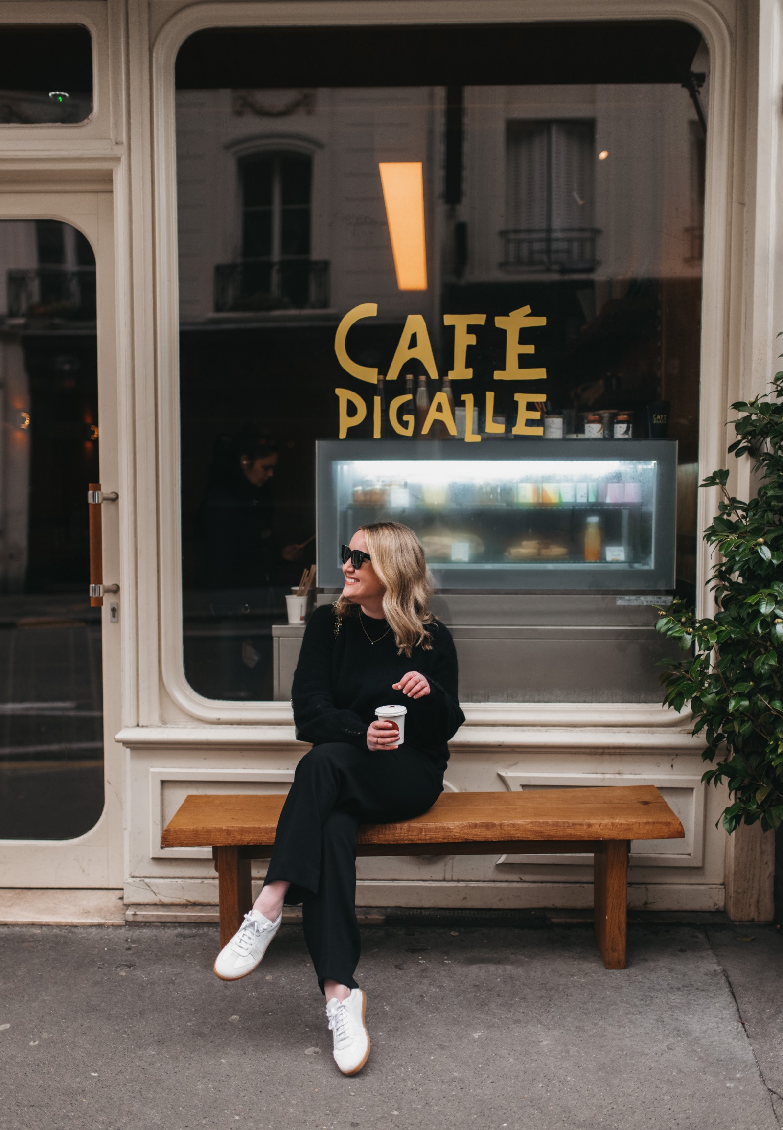 Woman wearing sneakers, jeans and blazer in Paris cafe, showcasing comfortable and stylish shoe choice for Europe