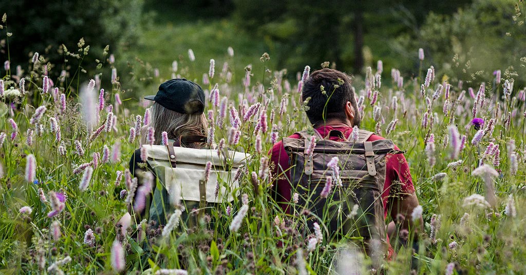 two hikers wearing vintage stylish canvas backpack with spacious main compartment and padded straps in a field of wild flowers