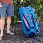 a man wearing flip flops standing beside a rolling duffle bag