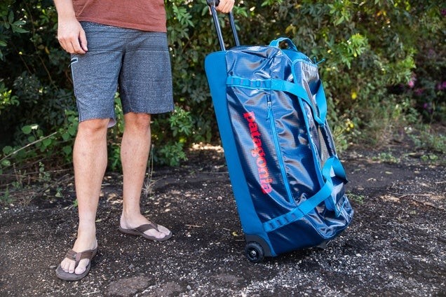 a man wearing flip flops standing beside a rolling duffle bag