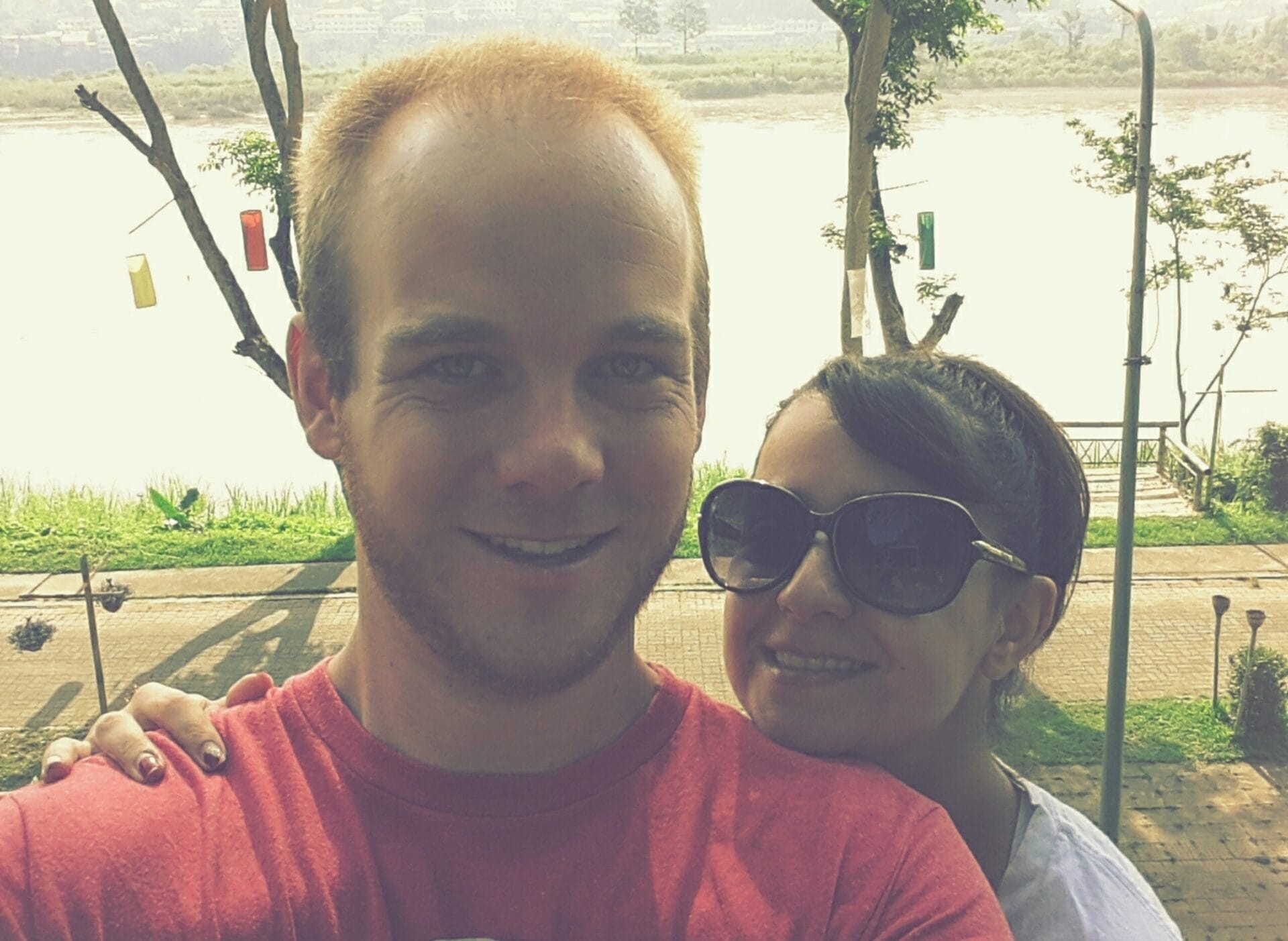 A couple taking a selfie in Chiang Khong, Thailand with Mekong river and greenery in the background.