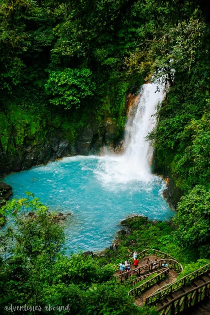 A waterfall pours into a bright blue river surrounded by lush green jungle in Costa Rica.