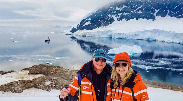 A couple stands in an Antarctic landscape at Neko Harbour, with snow-covered mountains and icy waters surrounding them.