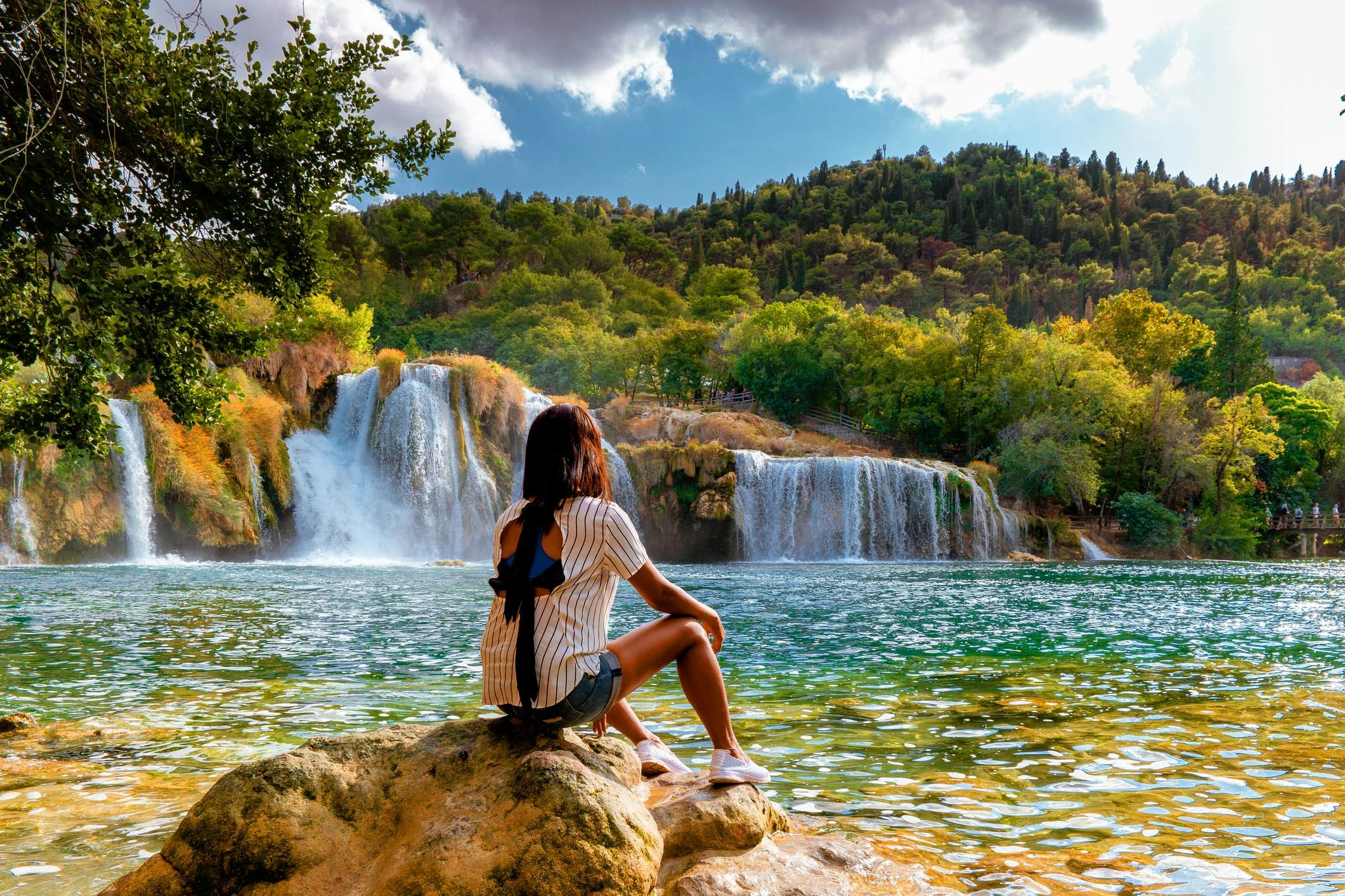 A woman sits on a rock at the edge of a pool being fed by a series of waterfalls in Croatia