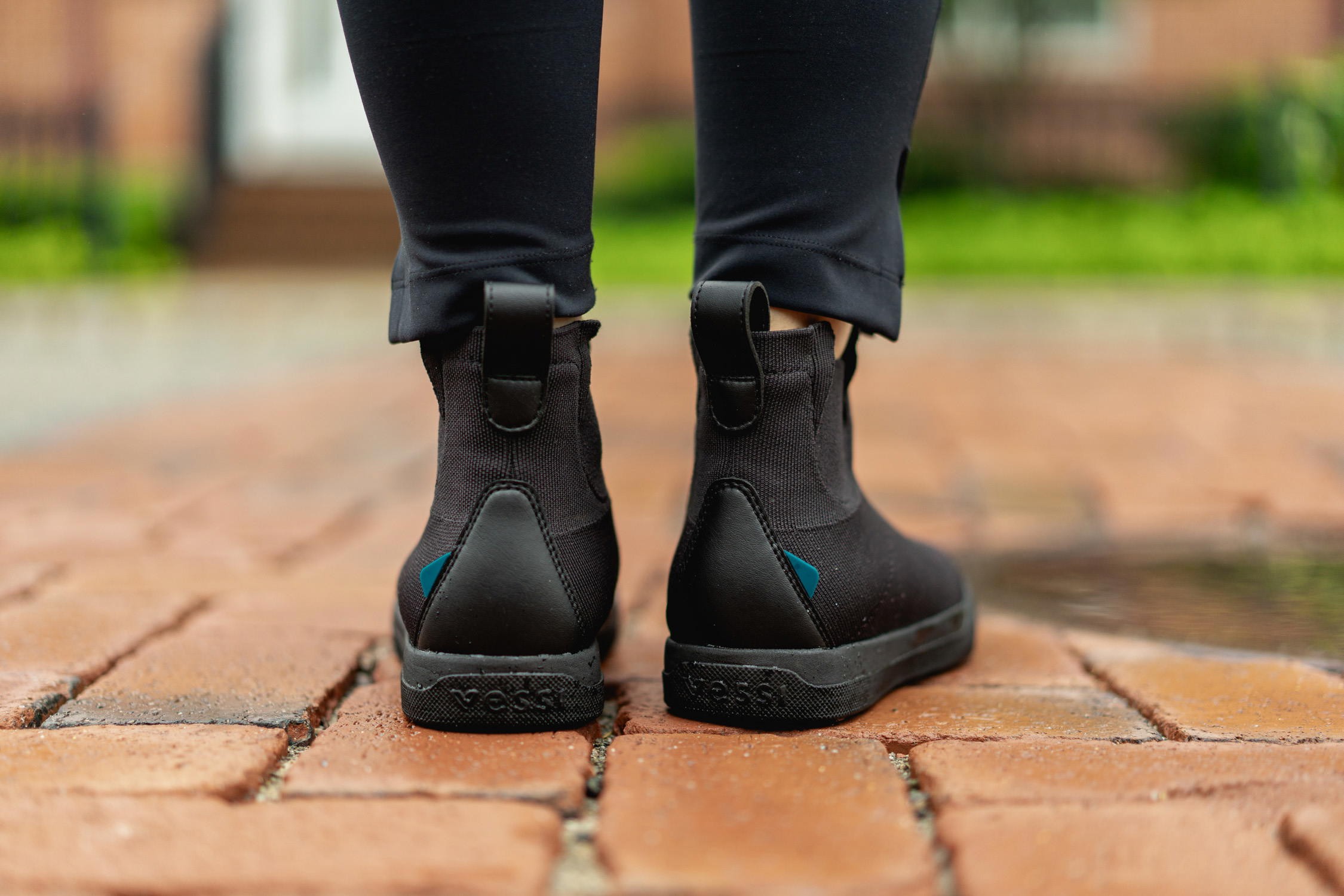 Man wearing white Vessi Weekend waterproof travel shoes standing on a wet street.