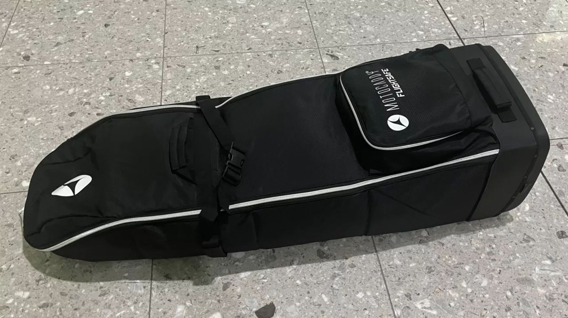 Motocaddy Flightsafe Travel Cover standing upright in an airport departure lounge, highlighting its protective padding