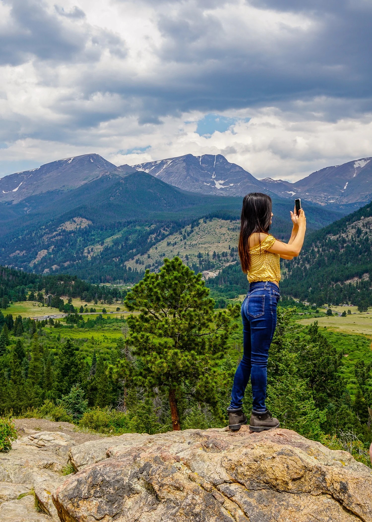 A woman overlooking a mountain vista, questioning if she is a traveler or traveller in Rocky Mountain National Park