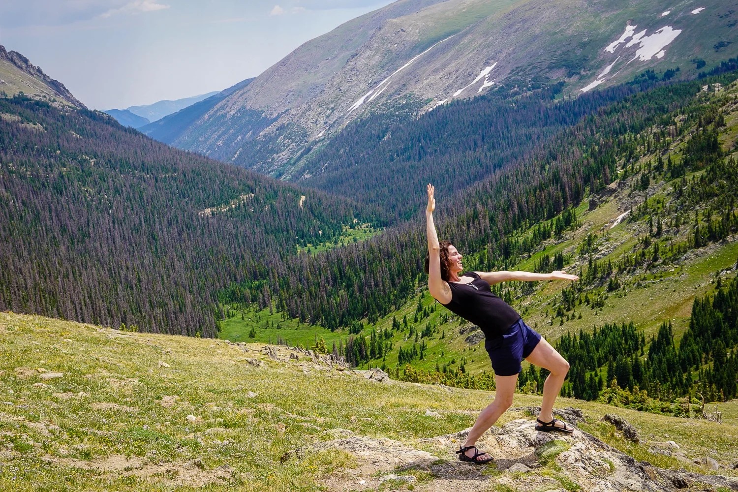 Woman standing in front of snowy mountains, pondering the spelling of traveler or traveller