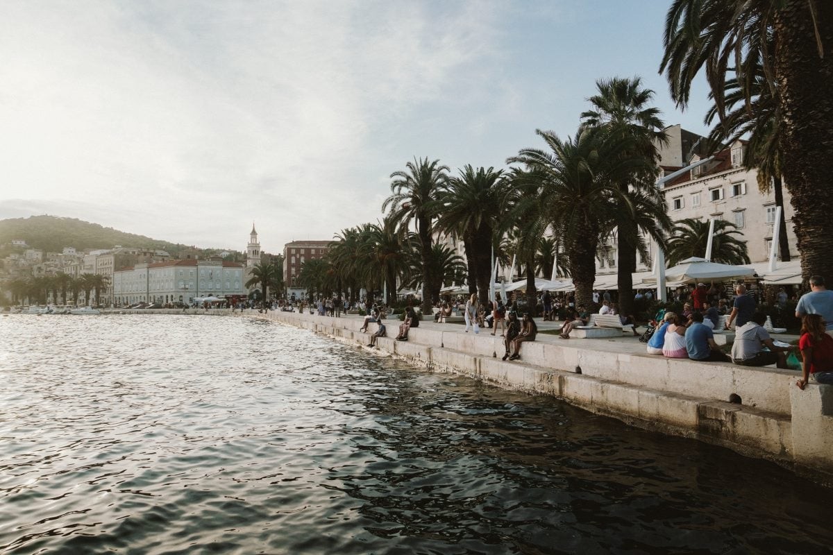 Lively Riva promenade in Split, lined with cafes and palm trees, leading to the historic Diocletian's Palace, a must-see in a Croatia travel itinerary.