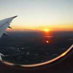 The wing of an airliner and a sunset over an urban landscape are visible from a window seat