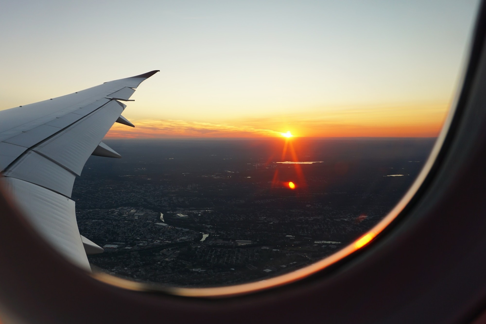 The wing of an airliner and a sunset over an urban landscape are visible from a window seat