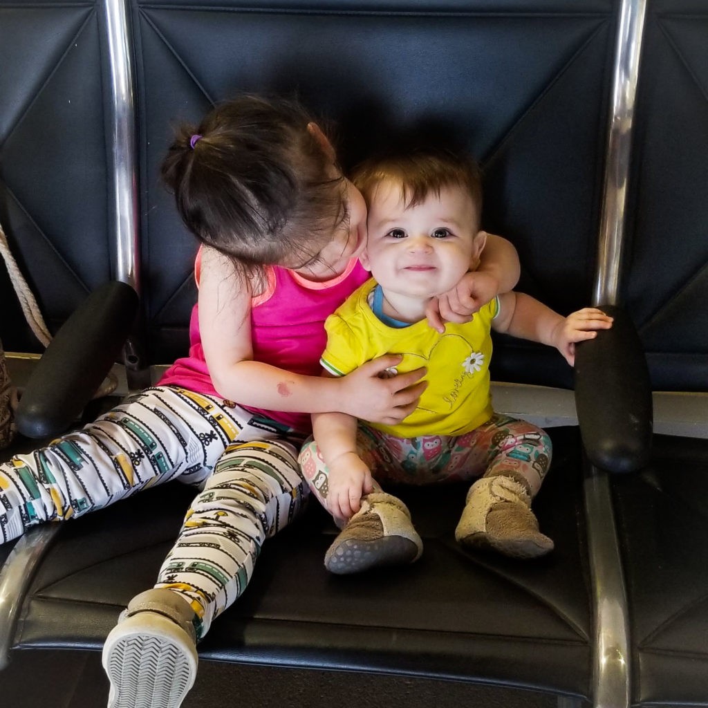 toddler holding baby in airport chairs