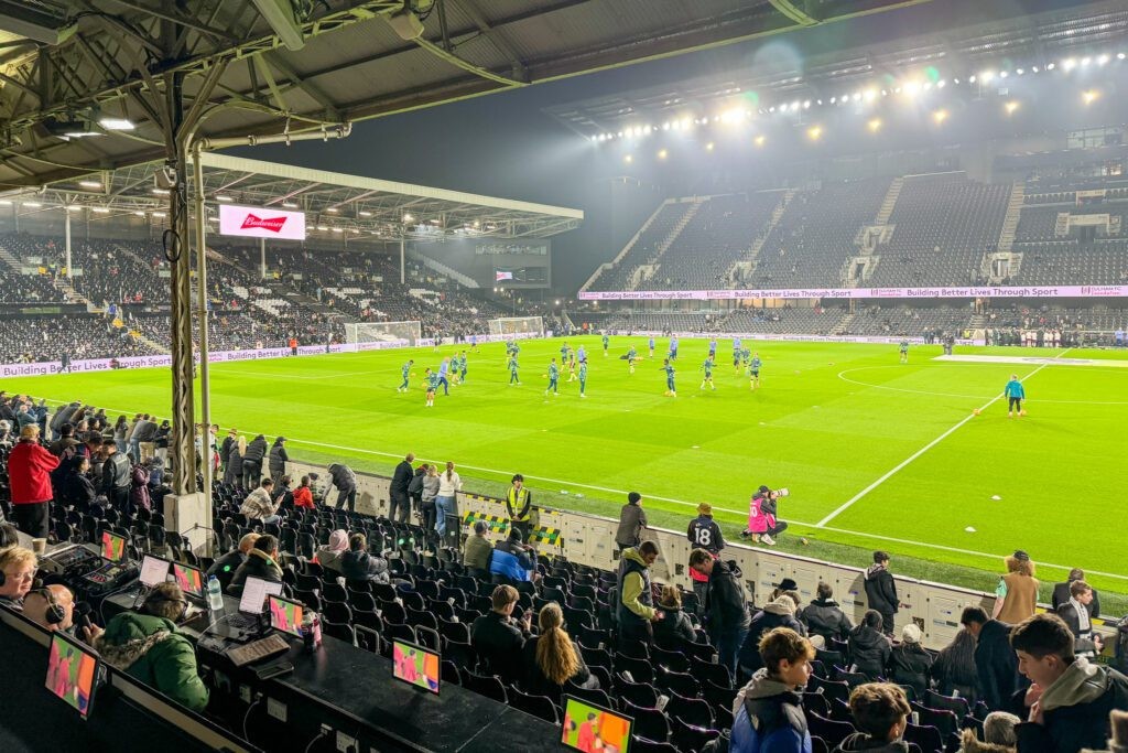 A football (soccer) game at Craven Cottage stadium in London, with fans cheering and players on the pitch