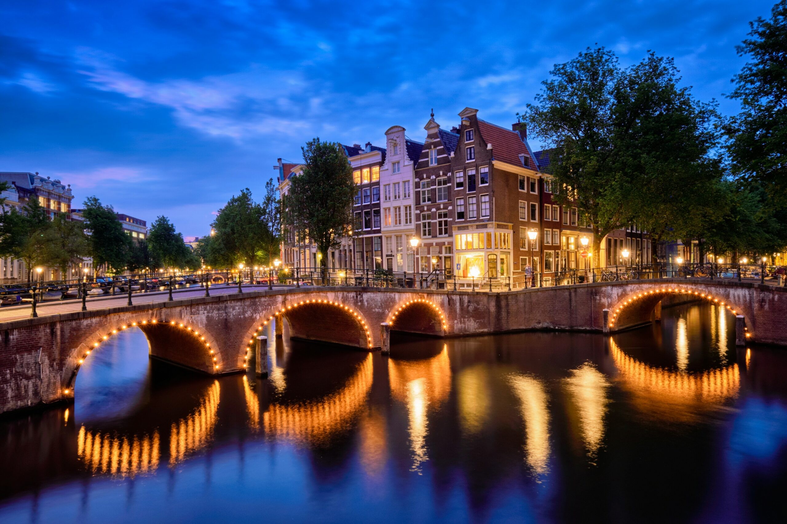 Amsterdam canal illuminated at night, reflecting city lights, representing a charming and romantic European city for an anniversary trip