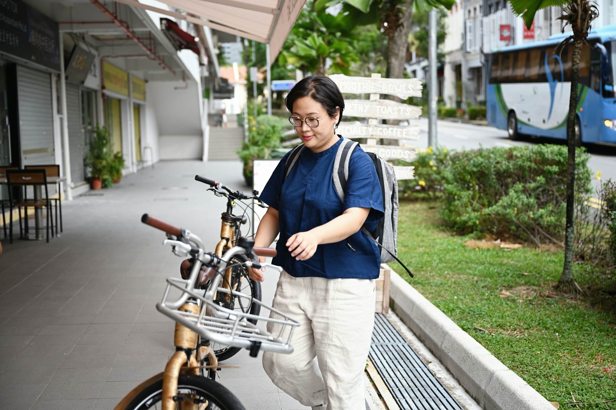 A woman with a backpack walking with a bicycle in a park in Singapore