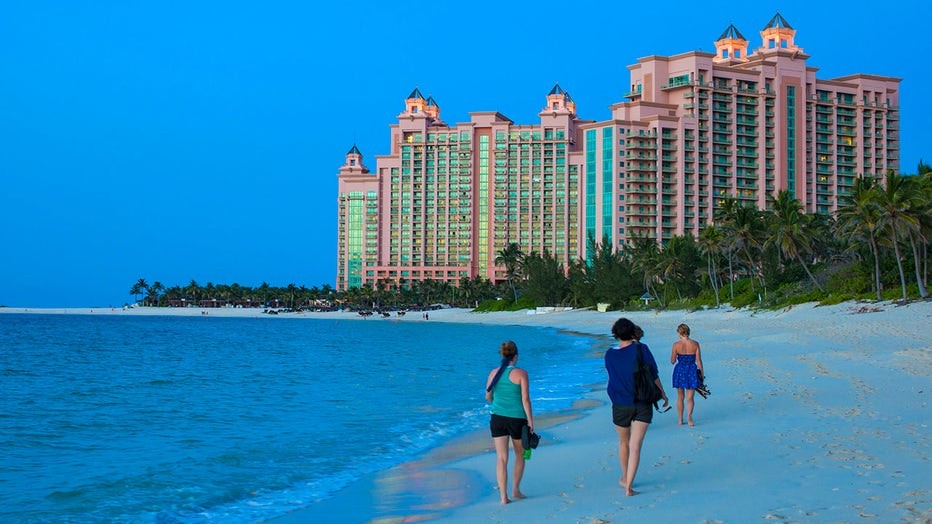 Tourists walking on Paradise Island beach towards Atlantis Hotel in Nassau, Bahamas, a popular destination where increased caution is advised due to recent travel advisory.