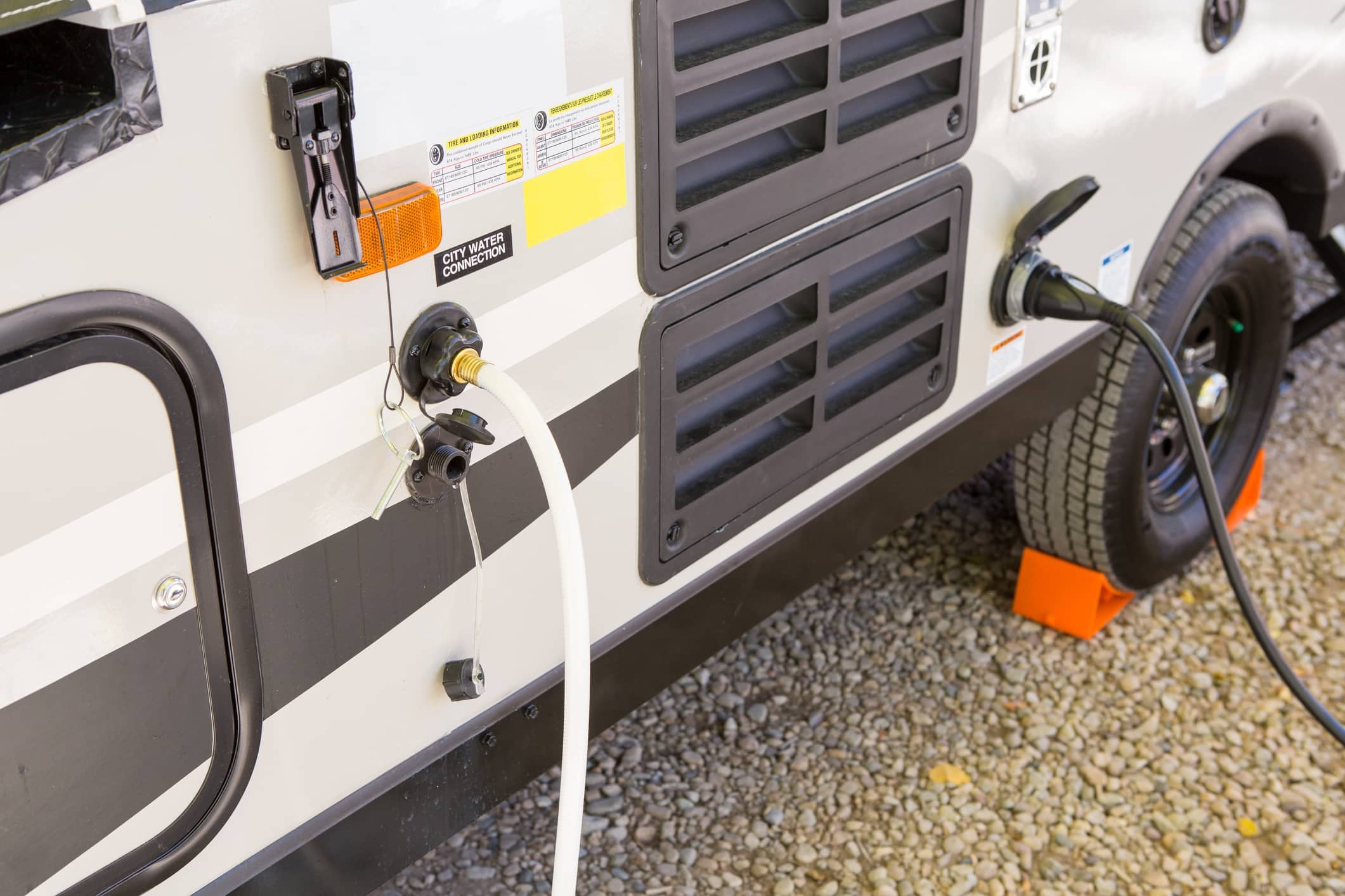 Filling a travel trailer fresh water tank in a scenic campground, highlighting the contrast with city water connection scenarios requiring pressure regulation