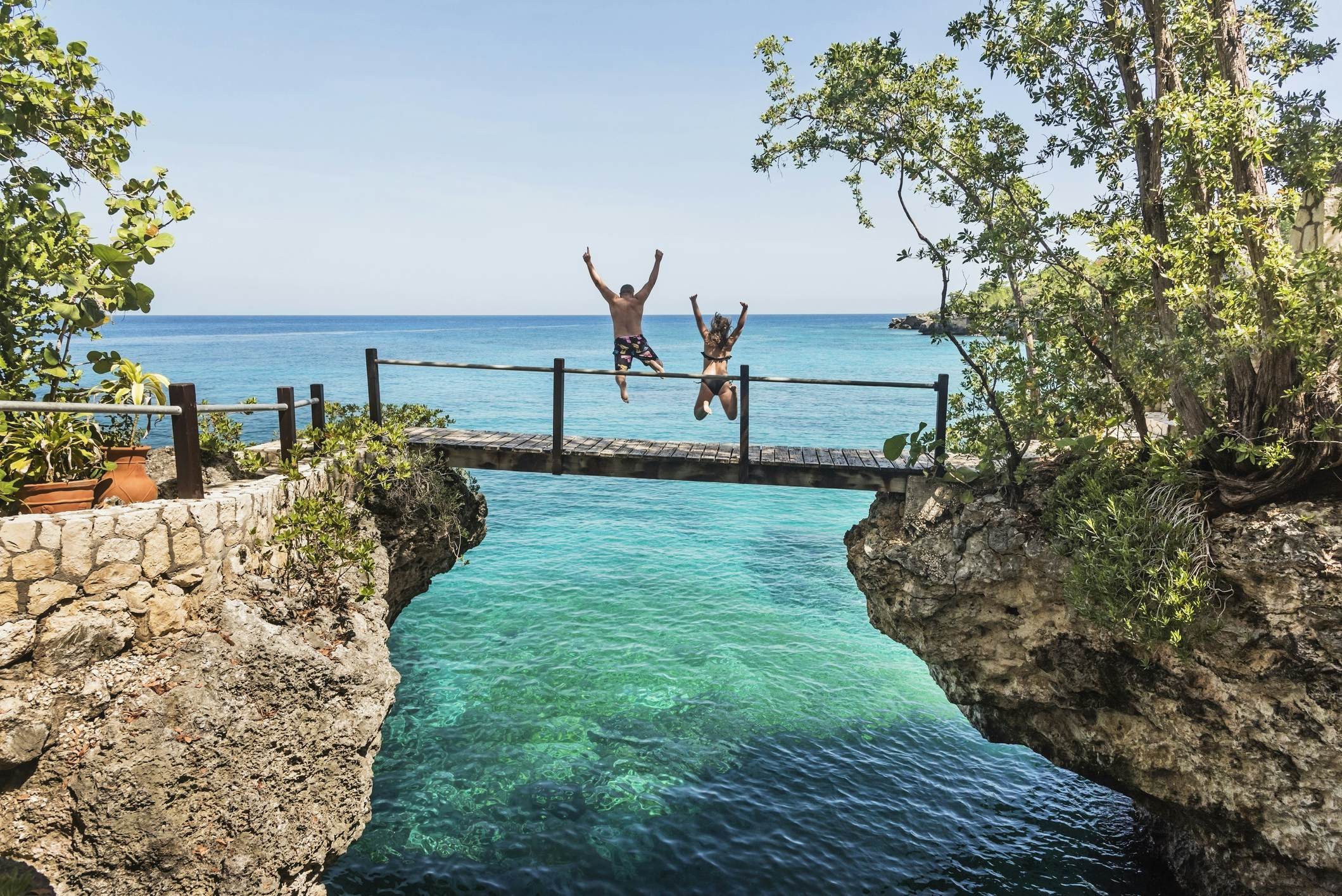 A woman and man jumping off a footbridge into the sea in Negril, Jamaica