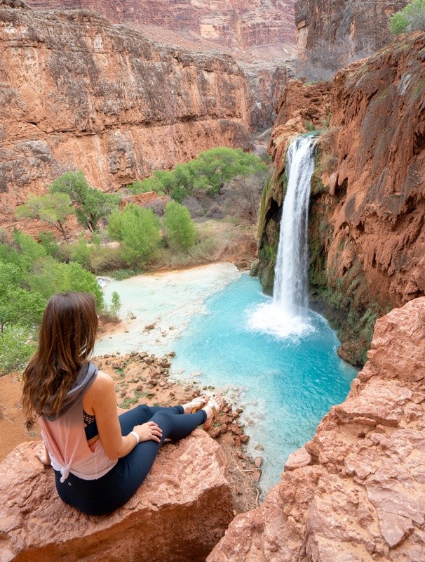 Hiker descending to Havasu Falls with turquoise blue water and red canyon walls