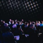 Dozens of people attentively participate in a corporate seminar, taking notes in a dimly lit auditorium.