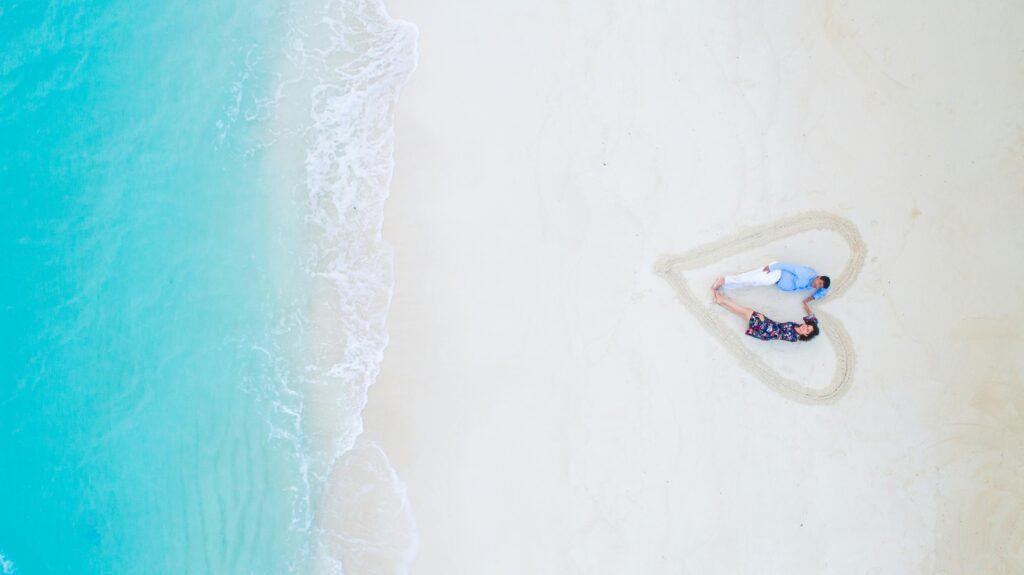 A couple on a honeymoon beach within a sand heart, representing safe travel wishes for special occasions like honeymoons