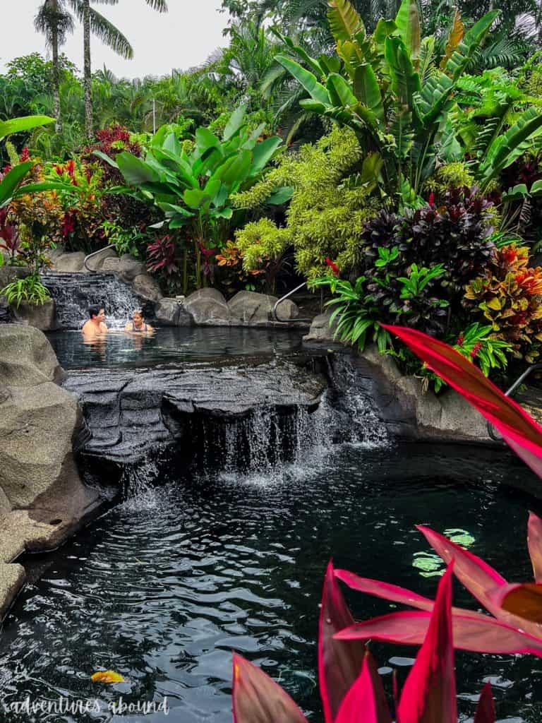 Two people sitting in a hot spring pool in La Fortuna, surrounded by lush nature. 