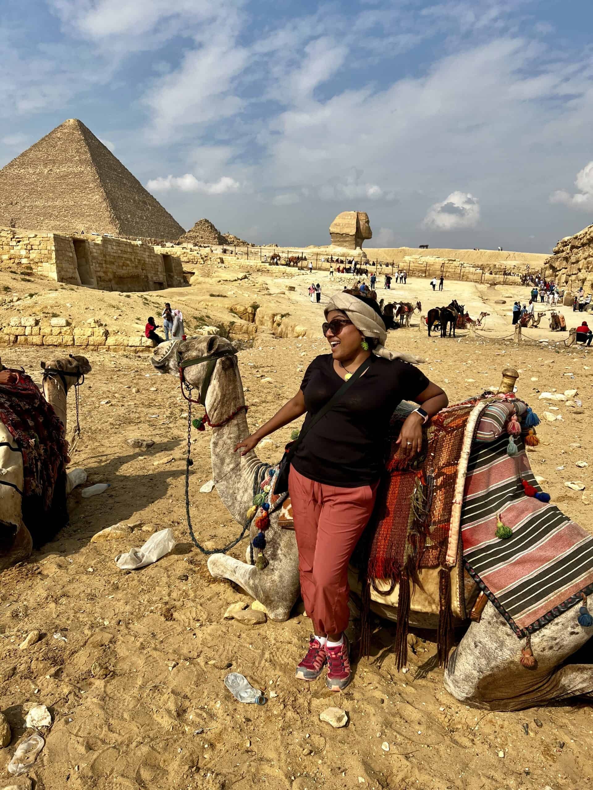 Woman in a blue long-sleeve shirt and beige capri pants standing in front of Egyptian pyramids, showcasing modest and practical travel wear for women.