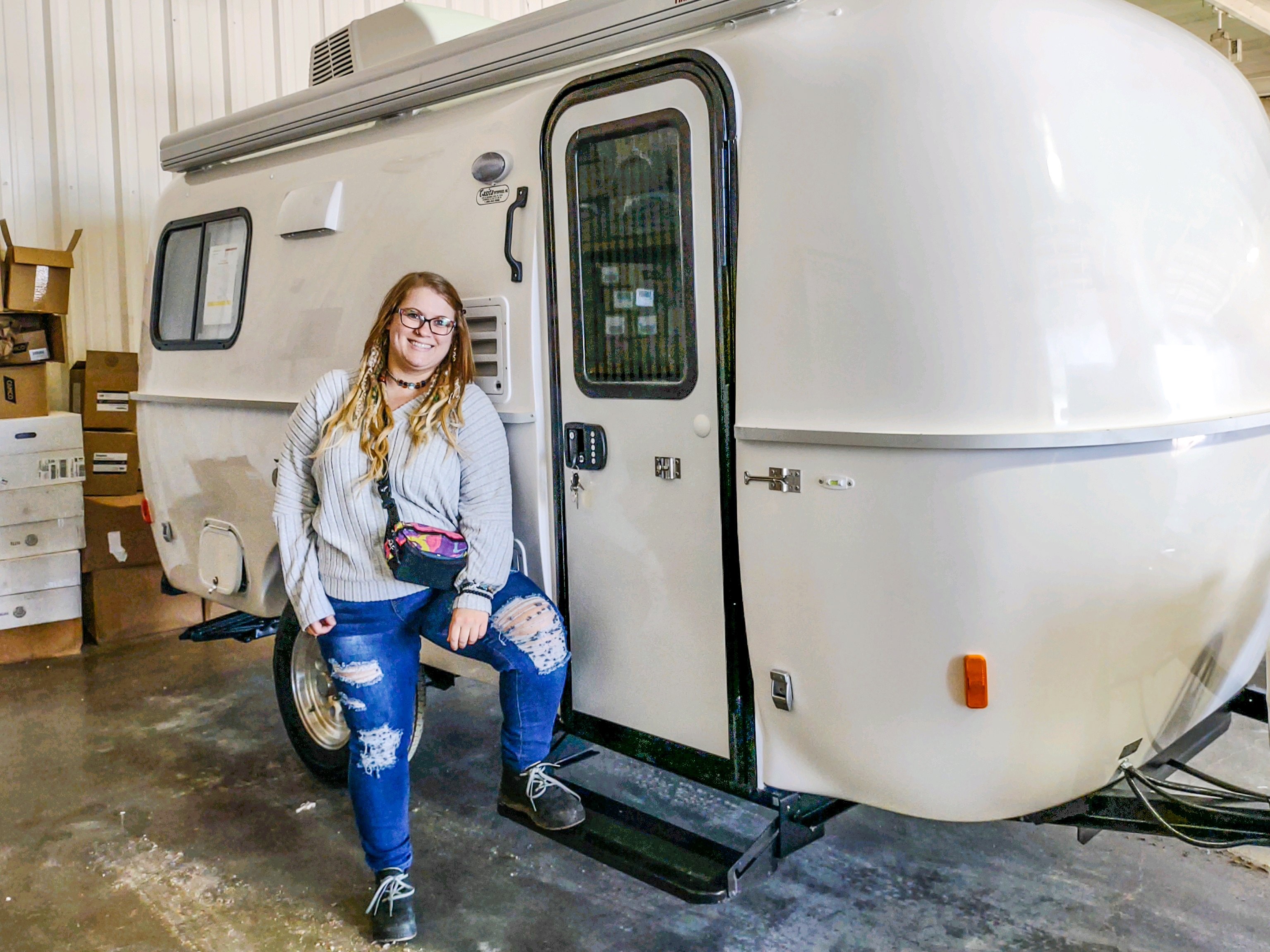 A woman smiling and holding keys in front of her new Casita travel trailer, celebrating her purchase.