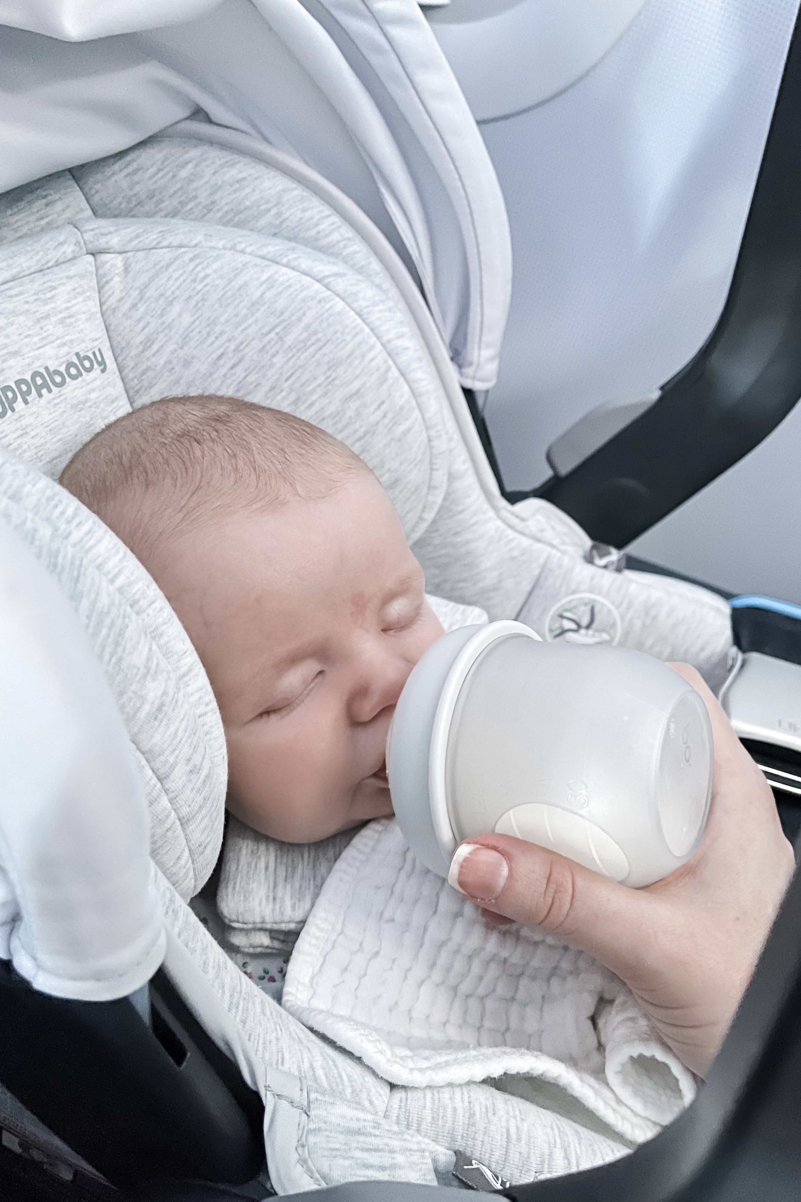 Mother holding a baby in a carrier on an airplane, suggesting comfort and closeness during air travel.