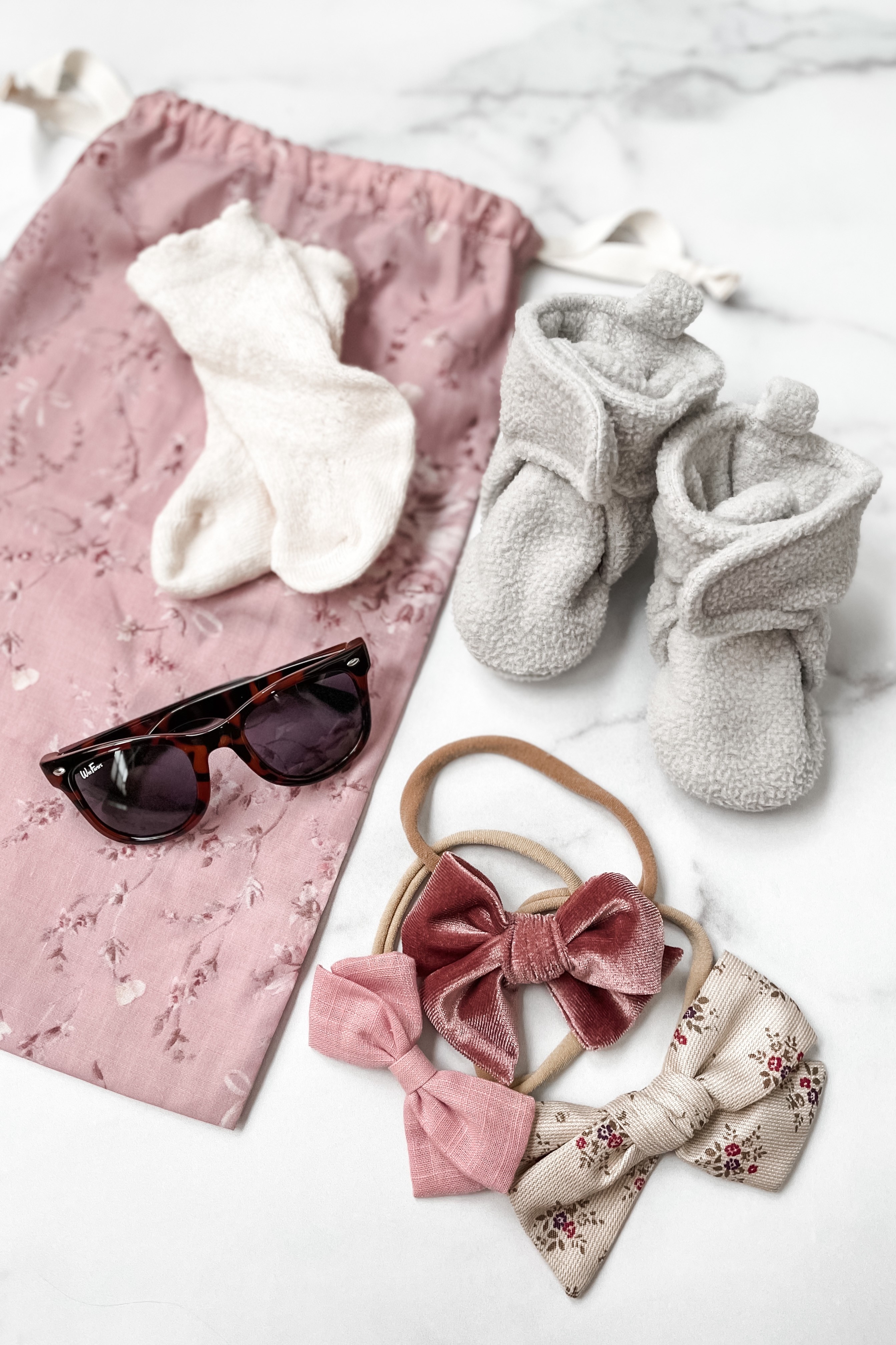 Drawstring bag filled with baby accessories like sunglasses, socks, and hair bows, demonstrating organized packing for small items.