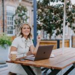 woman in a white jumpsuit sitting at a picnic table with her laptop