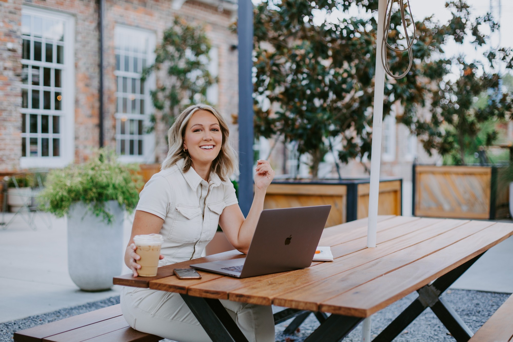 woman in a white jumpsuit sitting at a picnic table with her laptop