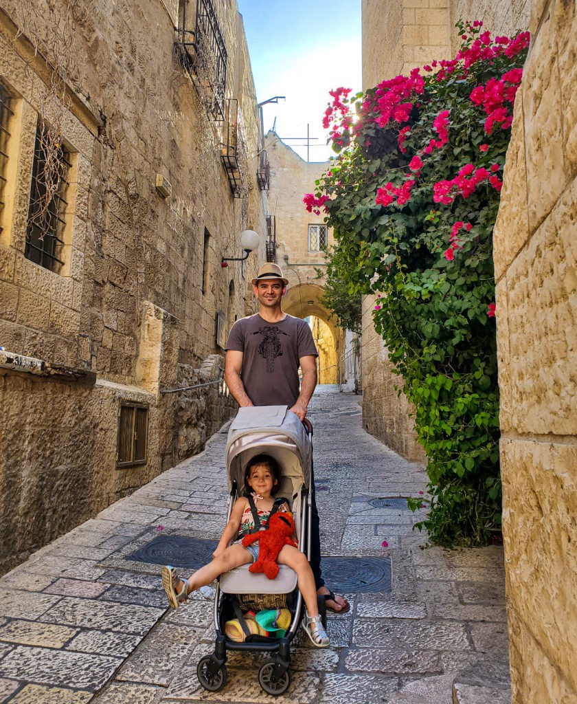 man pushing uppababy minu stroller with toddler holding elmo doll on cobbled road