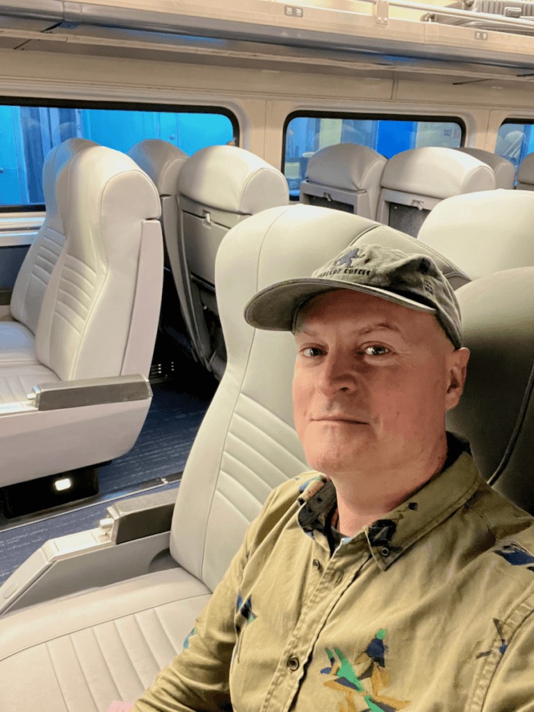 Traveler Matthew Kessi enjoys the journey in an Amtrak train car, highlighting the comfortable seating and scenic views on the Vancouver to Seattle route.