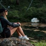 women sitting on a rock near a mountain lake wearing a vintage light blue canvas and leather backpack with padded shoulder straps