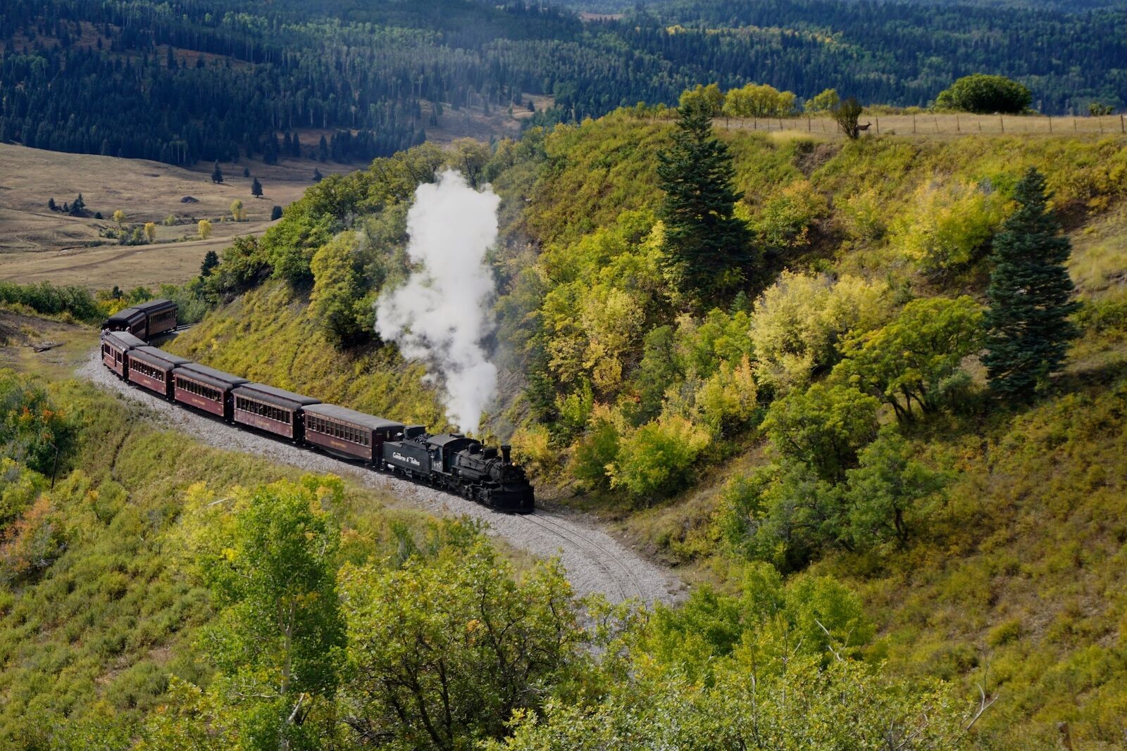 alt text: Rocky Mountaineer train with glass dome car traveling through red rock landscape