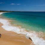 Makena beach in Maui, Hawaii, showcasing golden sand and clear blue water, with gentle waves lapping the shore, palm trees swaying in the background, and a clear sky above, perfect for a spring vacation