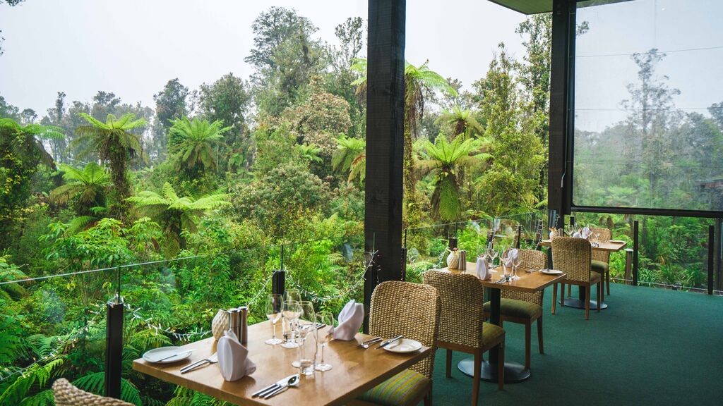 Luxurious dining area at Te Waonui Forest Retreat, New Zealand, surrounded by lush greenery, suggesting a secluded and nature-immersive anniversary getaway