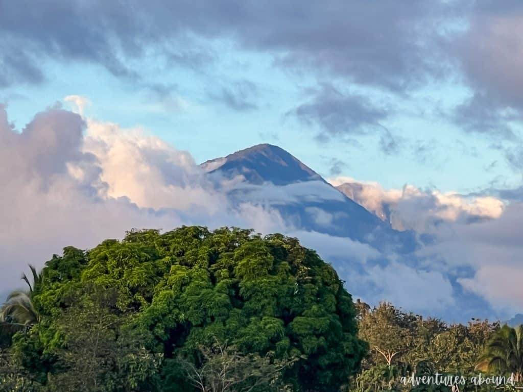 A mountain top coming out of the clouds in front of a tropical woody area. 